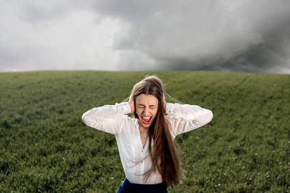 Woman holds hand to her head while crying in a field with cloudy sky.