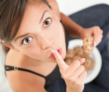 A woman holds her finger to her mouth as she enjoys a secret snack. 