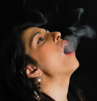 A girl, head tipped back, breathes smoke out into the air. 