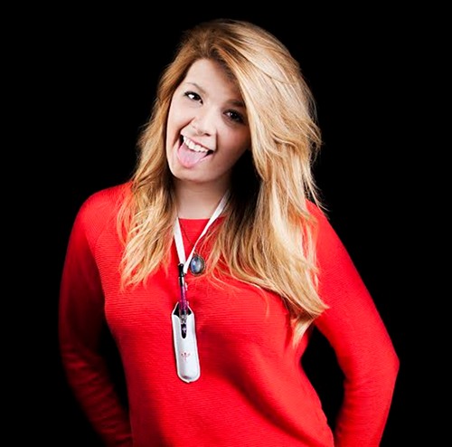Girl in red jumper sticks out her tongue. An ecigarette in a pouch lanyard sits on her chest.
