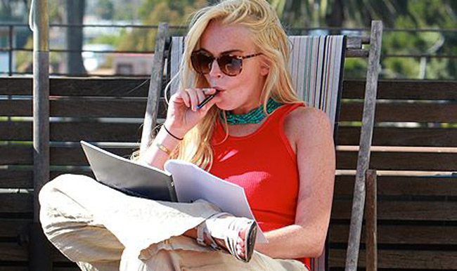 Lindsay Lohan sitting on a sunlounger with a vape in hand