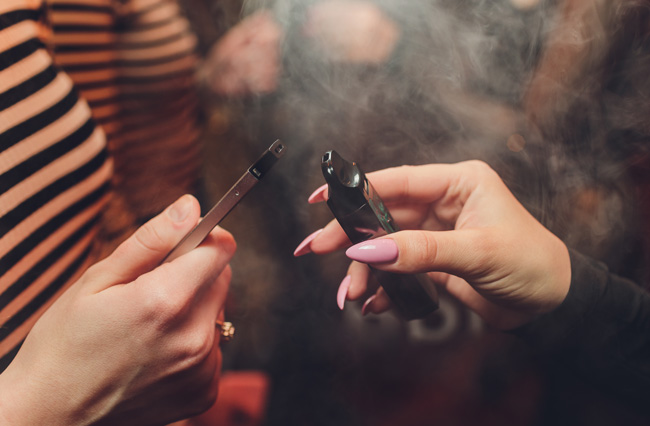 Friends comparing refillable and disposable vape devices in a club. 