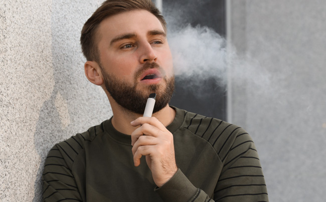 A man uses a disposable vape while leaning against the wall.