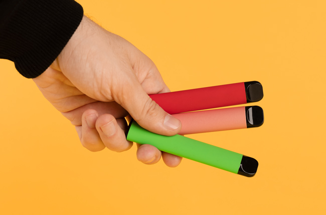 A hand holds disposable vape devices in different colours.